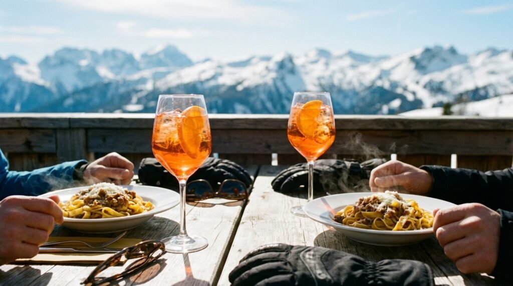 Skieurs déjeunant sur une terrasse ensoleillée dans les Dolomites, avec des verres d'Aperol Spritz et des plats de pâtes, face aux montagnes.
