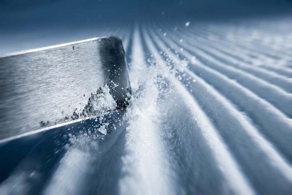 Gros plan sur la carre d'un ski alpin coupant la neige damée en virage carving, illustrant l'importance de la longueur de carre pour l'accroche.