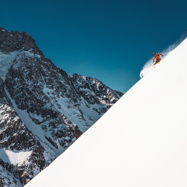 Skieur solitaire au sommet d'une pente raide vertigineuse dans les Alpes, prêt à s'élancer sur une piste noire mythique.