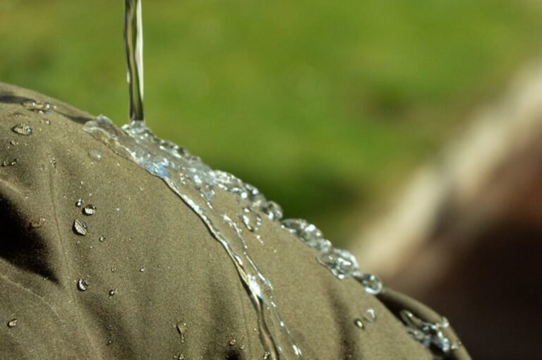 Une goutte d'eau perlant parfaitement sur la surface d'un tissu technique vert forêt, illustrant la déperlance et la tension superficielle.
