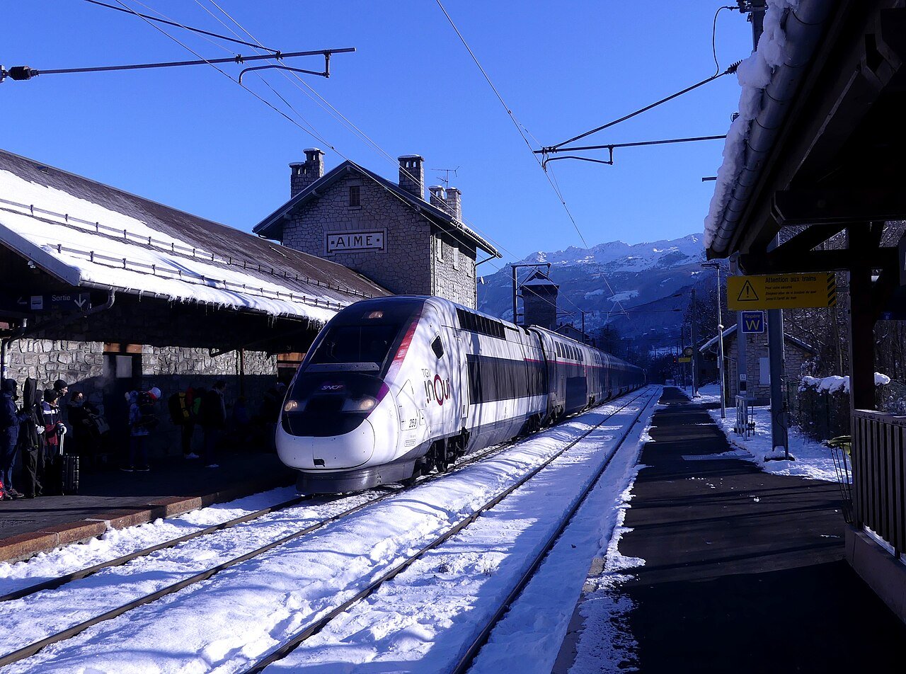 Un TGV stationné dans une gare enneigée des Alpes, illustrant le voyage en train direct vers les stations de ski sans voiture.