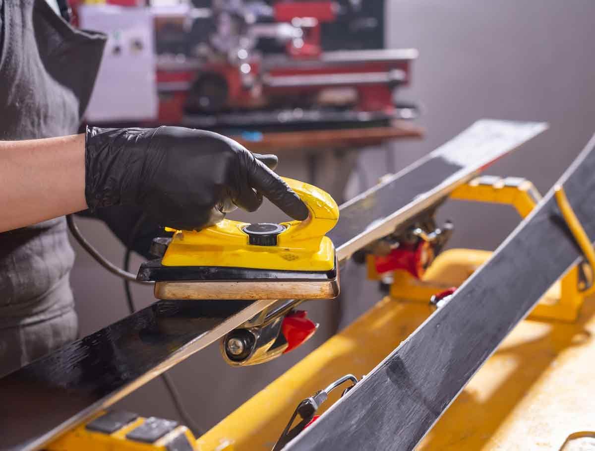 Gros plan sur un fer à farter professionnel faisant fondre un pain de fart chaud sur la semelle d'un ski alpin.