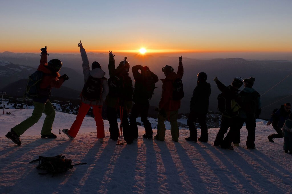 Festivaliers levant les bras devant une scène de concert lors d'un magnifique coucher de soleil sur les sommets alpins.