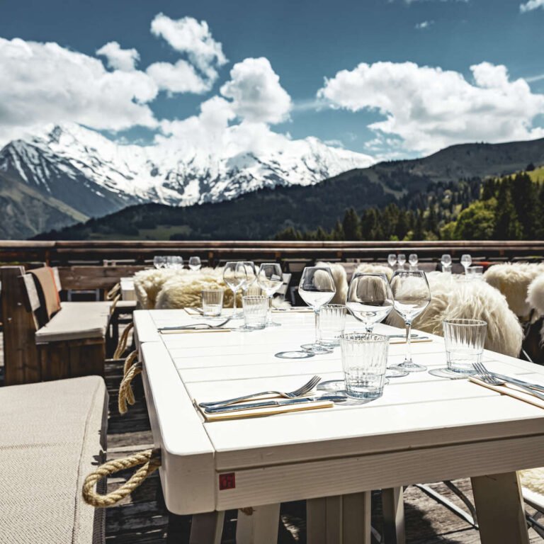 Skieurs profitant d'un déjeuner sur la terrasse ensoleillée d'un authentique chalet d'alpage en bois, loin des usines à ski de haute altitude.