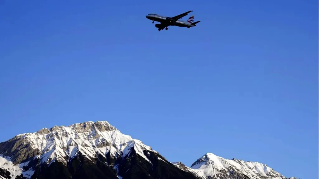 Un avion de ligne survolant la chaîne des Alpes, un mode de transport rapide mais lourd de conséquences écologiques et tarifaires.