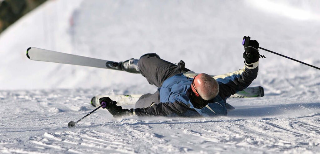 Skieur en pleine chute dans la neige, illustrant les forces de torsion extrêmes subies par l'articulation du genou si la fixation ne se déclenche pas.