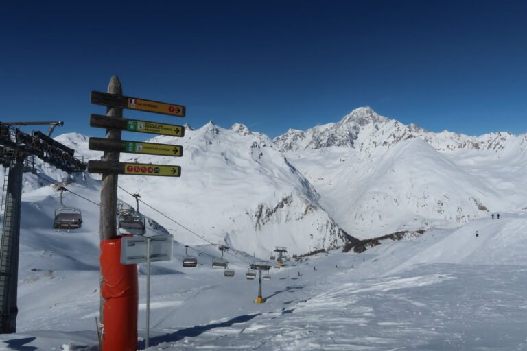 Skieur alpin au sommet d'un col enneigé, observant le panorama qui s'ouvre sur une vallée étrangère au-delà de la frontière.