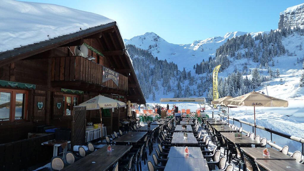 Table chaleureuse sur la terrasse ensoleillée d'un refuge d'altitude, prête à accueillir les skieurs pour un repas traditionnel.