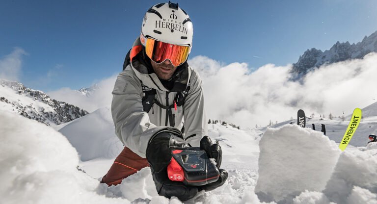 Gros plan sur un DVA (Détecteur de Victimes d'Avalanches) tenu en main par un skieur, l'outil électronique indispensable pour le hors-piste.