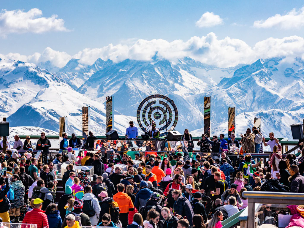 DJ mixant sur une immense scène en plein air face à une foule en délire, illustrant l'ampleur des festivals d'altitude.