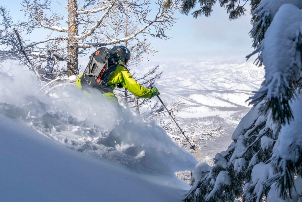 Skieur freeride dessinant de larges courbes dans une poudreuse profonde et sèche, typique du climat continental extrême.