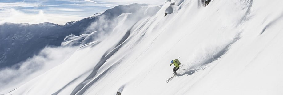 Skieur freeride évoluant dans une poudreuse profonde très légère loin des pistes damées, l'environnement type nécessitant l'équipement de sécurité.