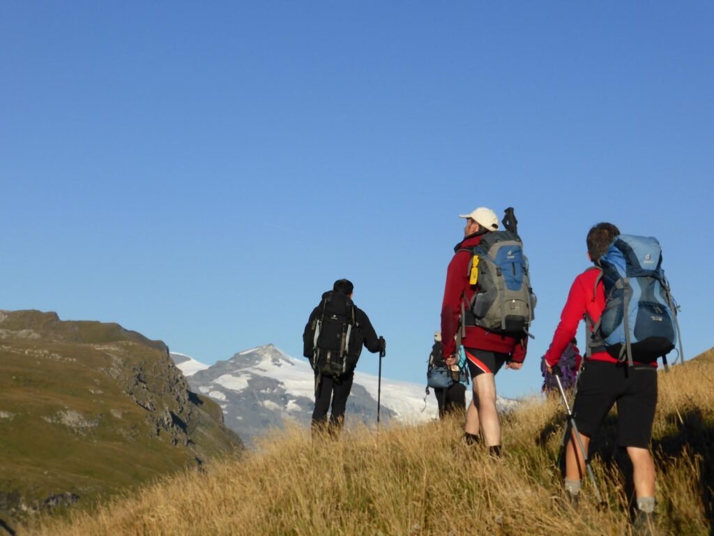 Groupe de randonneurs équipés de sacs à dos légers cheminant sur un sentier escarpé face aux sommets enneigés.