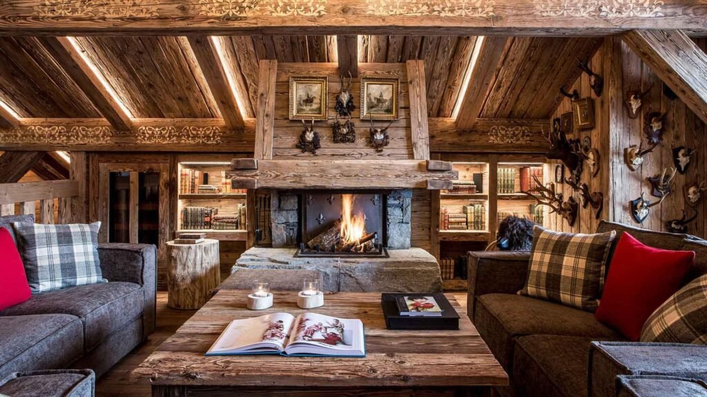 Intérieur chaleureux d'un refuge de montagne avec du mobilier en bois massif, un poêle à bois et une grande fenêtre donnant sur la neige.
