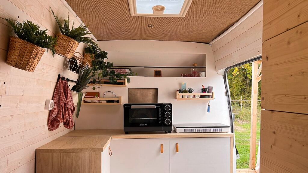 Intérieur douillet tout en bois d'un van aménagé, avec une vue sur la forêt enneigée depuis les portes arrière ouvertes.