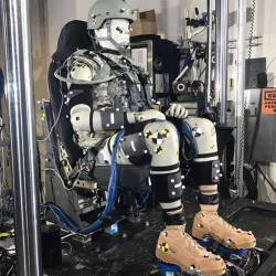 La tête d'un mannequin de crash-test bardée de capteurs, frappant une enclume en acier dans l'atmosphère confinée et sombre d'un laboratoire balistique.