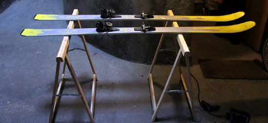Une vue macroscopique et sombre révélant le puissant ressort hélicoïdal et les mâchoires métalliques d'une fixation de ski de haute performance.