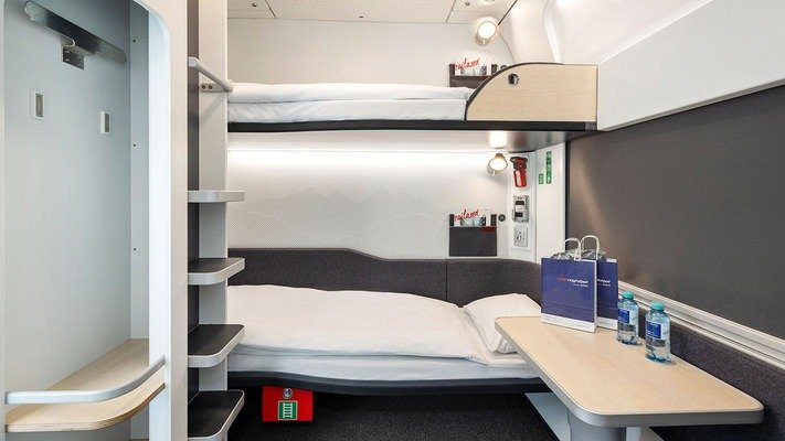 L'intérieur d'une cabine couchette moderne de l'ÖBB Nightjet, un cocon de voyage minimaliste Blanc & Gris Ardoise, optimisé pour le repos avant une journée de ski.
