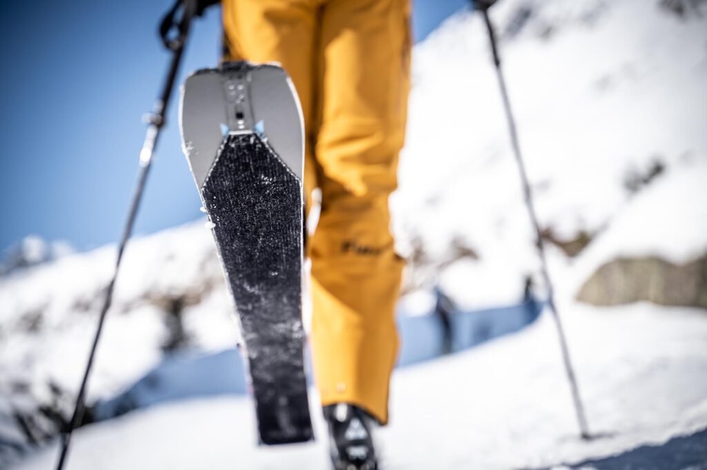 Gros plan sur des skis équipés de peaux de phoque creusant la toute première trace dans la poudreuse d'une pente raide.