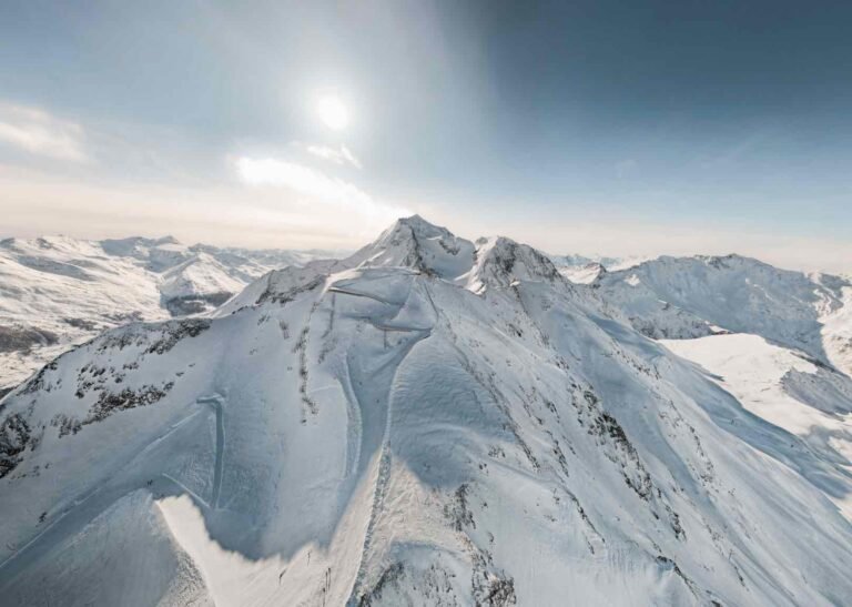 Une large piste de ski totalement déserte au petit matin, baignée par la lumière rasante du soleil levant dans la station des Arcs.