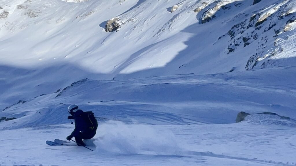 Skieur solitaire traçant de belles courbes dans la poudreuse vierge au petit matin, sublimé par la lumière dorée du lever de soleil.