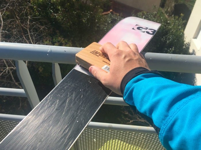 Un technicien utilise une raclette en plexiglas pour retirer l'excédent de fart refroidi sur la semelle du ski.
