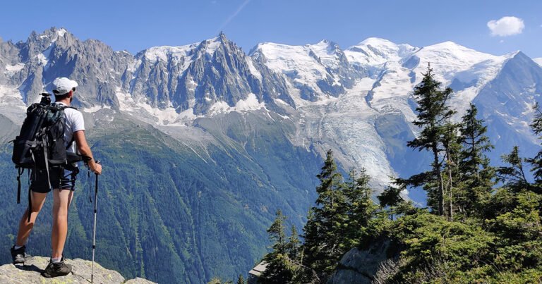 Un randonneur solitaire contemplant la vallée de Chamonix et les glaciers depuis un sentier d'altitude du Tour du Mont-Blanc.