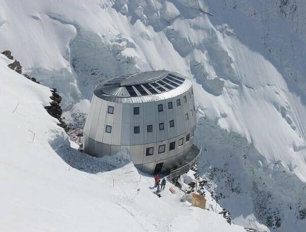 Petit refuge en pierre et en bois perché sur un éperon rocheux au milieu des glaciers alpins enneigés.