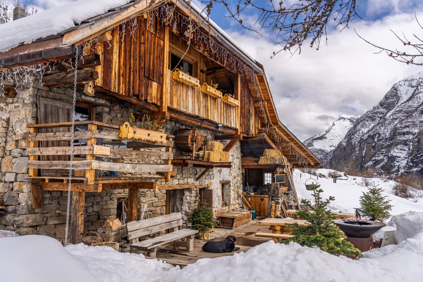 Petit chalet refuge en bois isolé sous la neige en haute montagne à la tombée de la nuit, avec les sommets en arrière-plan.