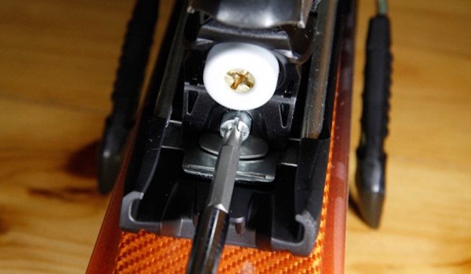 Gros plan sur l'utilisation d'un tournevis cruciforme pour ajuster la vis de tension du ressort (le DIN) sur la butée avant d'une fixation de ski alpin.