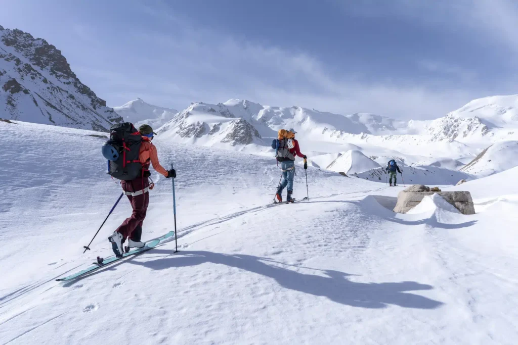 Skieurs de randonnée équipés de peaux de phoque gravissant une pente immaculée dans le silence absolu de la montagne.