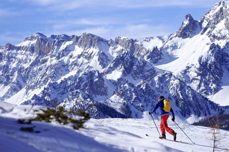Skieur de randonnée s'élevant dans un vallon immaculé et désert du Parc Naturel Régional du Queyras sous un ciel bleu d'hiver.
