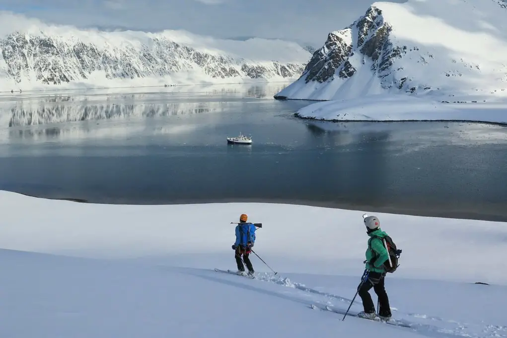 Un skieur de randonnée contemplant l'immensité de l'océan Arctique depuis une crête enneigée de l'archipel du Svalbard.