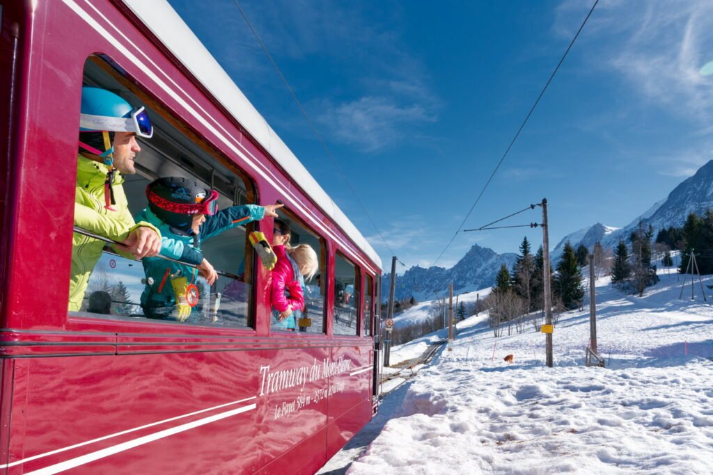 Skieur descendant d'un train en gare alpine avec son matériel, marquant le début d'un séjour aux sports d'hiver sans aucun stress routier.