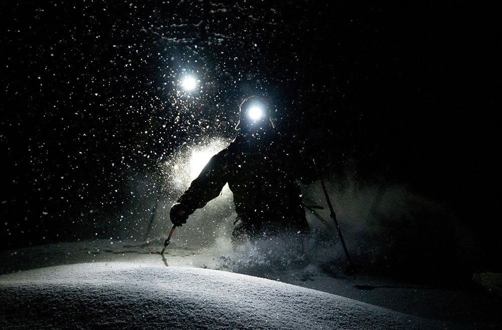 Skieur dévalant une pente dans l'obscurité, guidé par les faisceaux lumineux des projecteurs de la station.