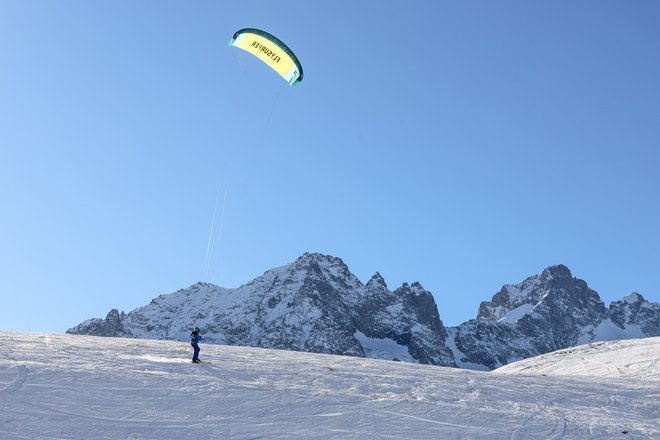 Skieur tracté par une grande voile de snowkite sur une vaste étendue enneigée immaculée.