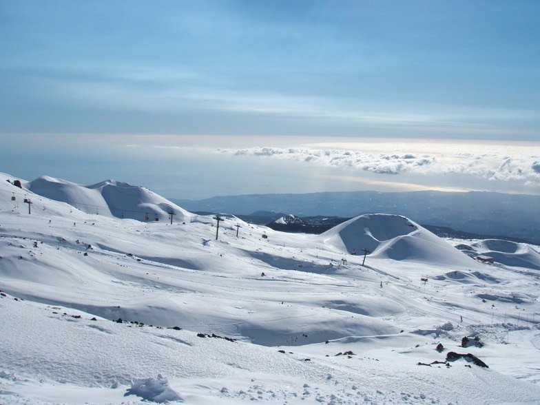Un skieur sur les remontées mécaniques de l'Etna, profitant d'une vue dégagée vertigineuse sur les eaux bleues de la mer Ionienne.