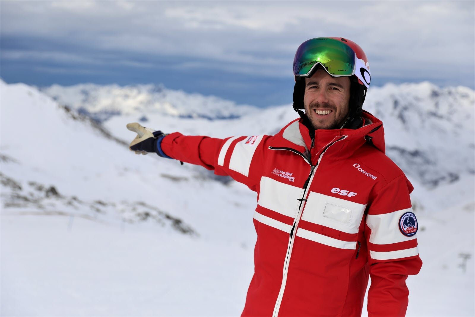 Skieur de dos portant une veste rouge éclatante face aux montagnes enneigées, rappelant l'uniforme emblématique des moniteurs de ski français.