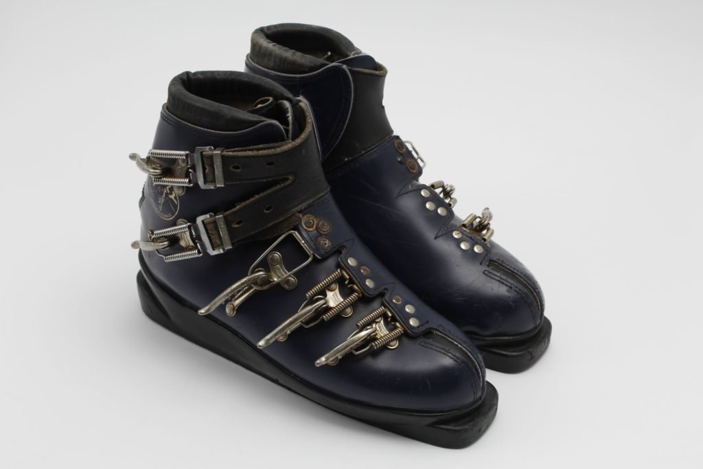 Ancienne paire de chaussures de ski en cuir marron à lacets, posée sur la neige, symbole de l'inconfort des pionniers.