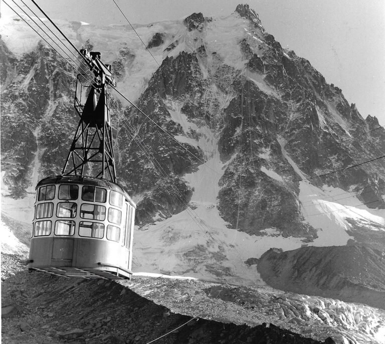 Ancienne cabine de téléphérique suspendue dans le vide au-dessus des cimes enneigées du massif du Mont-Blanc.