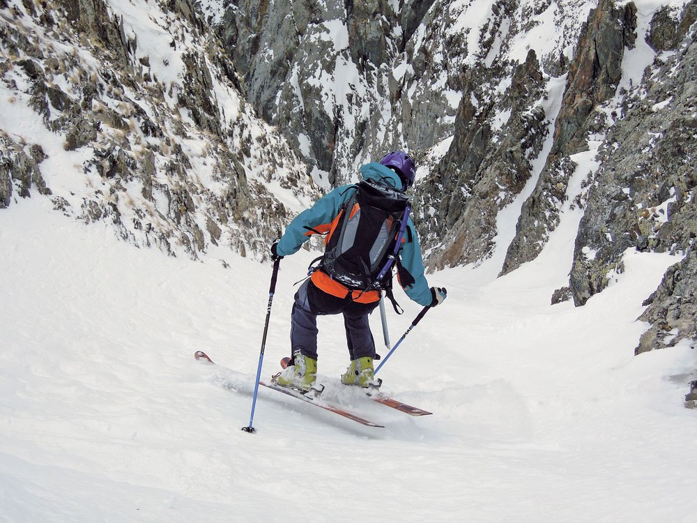 Exécution parfaite d'un virage sauté dans un couloir étroit par un skieur d'époque, le buste tourné vers le vide.