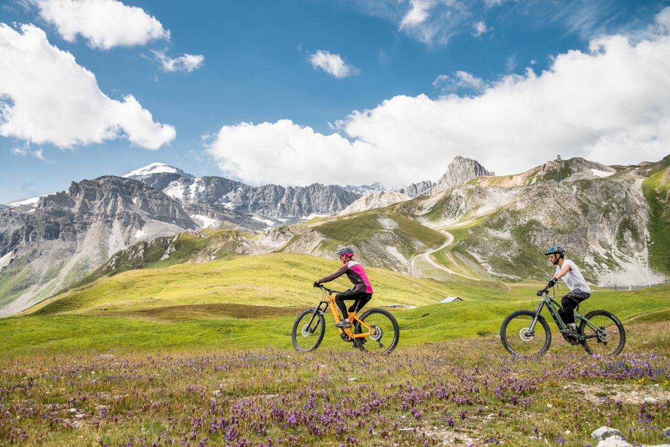 Vététiste dévalant une piste de descente engagée en pleine montagne, illustrant la transition des stations vers les sports d'été.