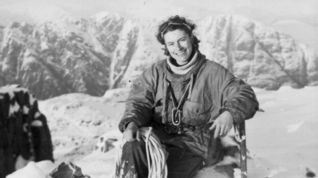 Une alpiniste souriante assise avec une corde devant des montagnes enneigées