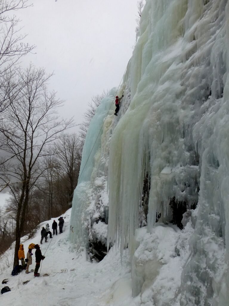 Grimpeur progressant à la verticale sur une cascade de glace avec outils et crampons