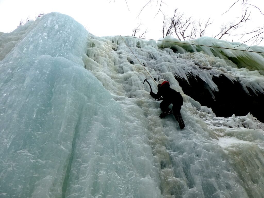 Grimpeur de cascade de glace utilisant deux outils à glace sur une paroi verticale