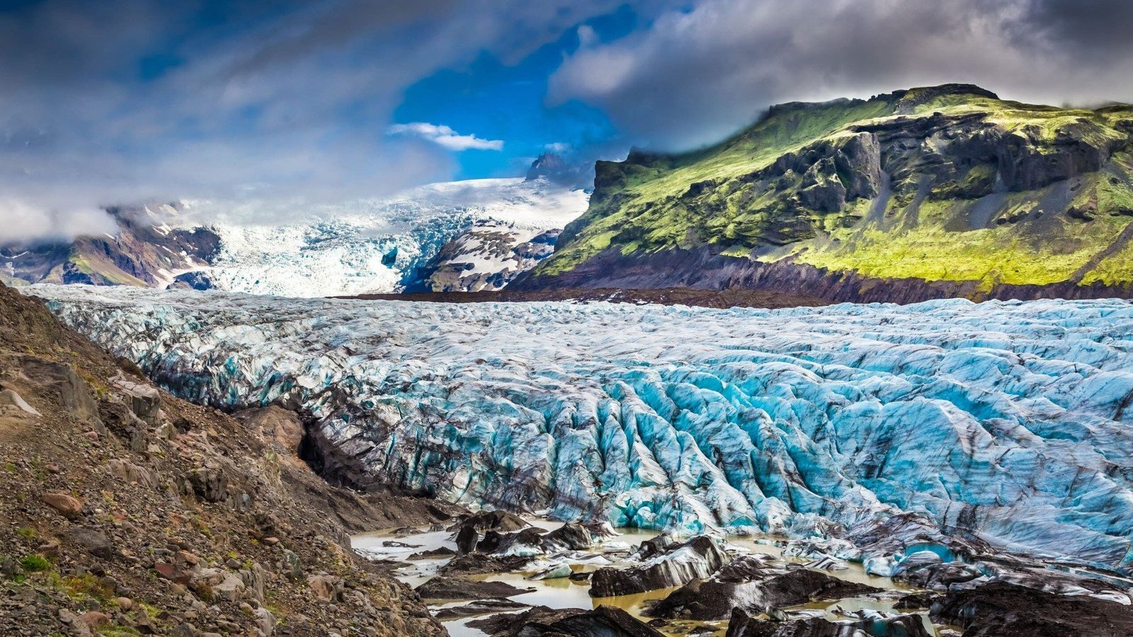 Glacier bleu crevassé bordé de montagnes rocheuses et verdoyantes